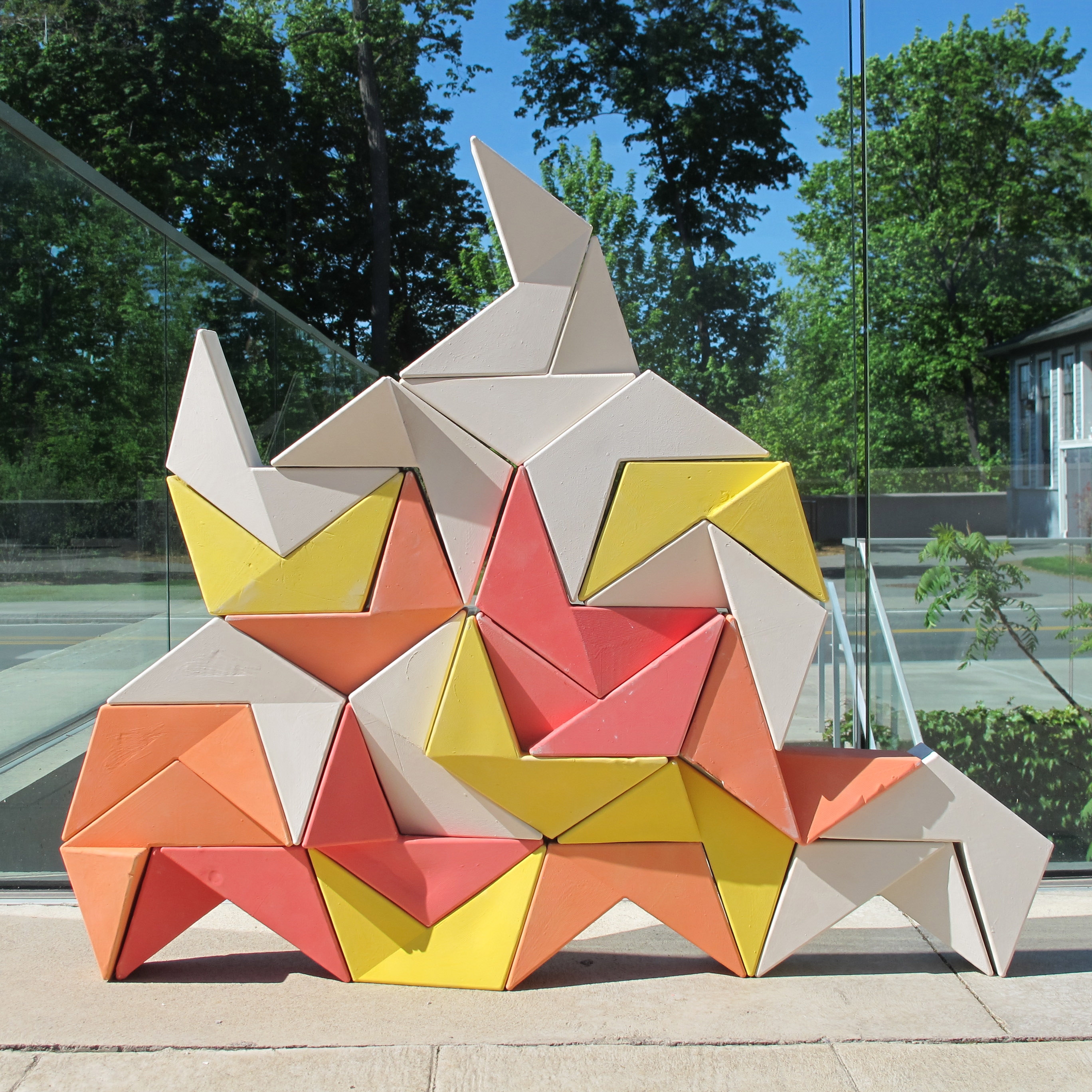 Colorfully glazed "bricks", the folded trapezoid shapes are interlocked in a miniature wall.